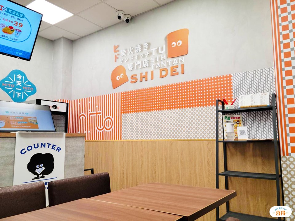 喜得店面照片，牆上有喜得吉祥物炭炭，有座位及點餐櫃檯，櫃台上方有電子看板，右下方有喜得的LOGO