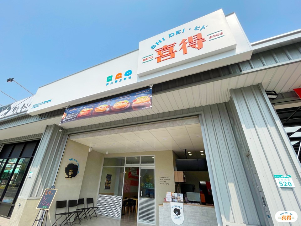 喜得的新形象日式店面,牆上有喜得吉祥物炭炭,門口有擺著幾張椅子供外帶的客人暫時坐著,右下角有喜得的LOGO