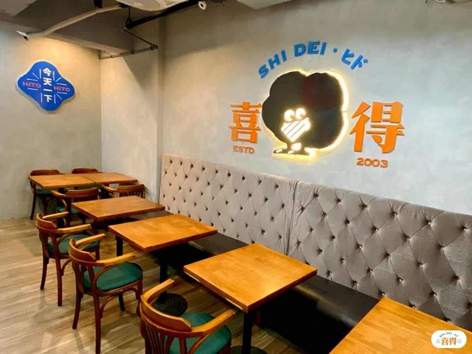 喜得炭火燒三明治的新形象日式店面，擺放許多桌椅，牆上有喜得吉祥物炭炭。右下角有喜得的LOGO